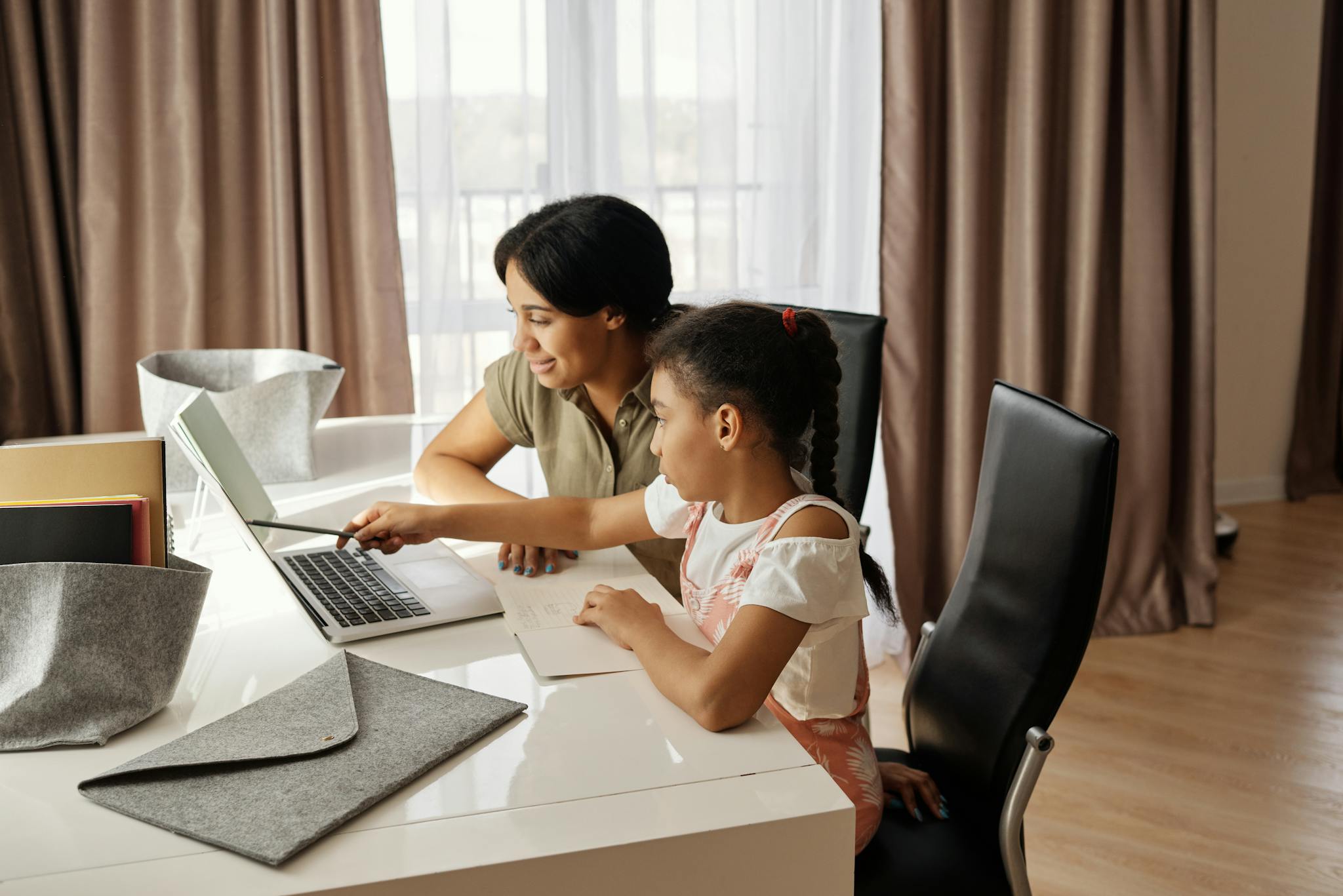 A mother assisting her daughter with online learning on a laptop, promoting education and family bonding.