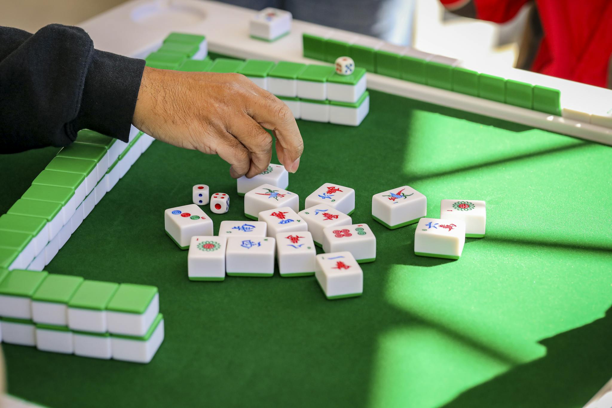 Hand arranging mahjong tiles during an intense game on a green table.